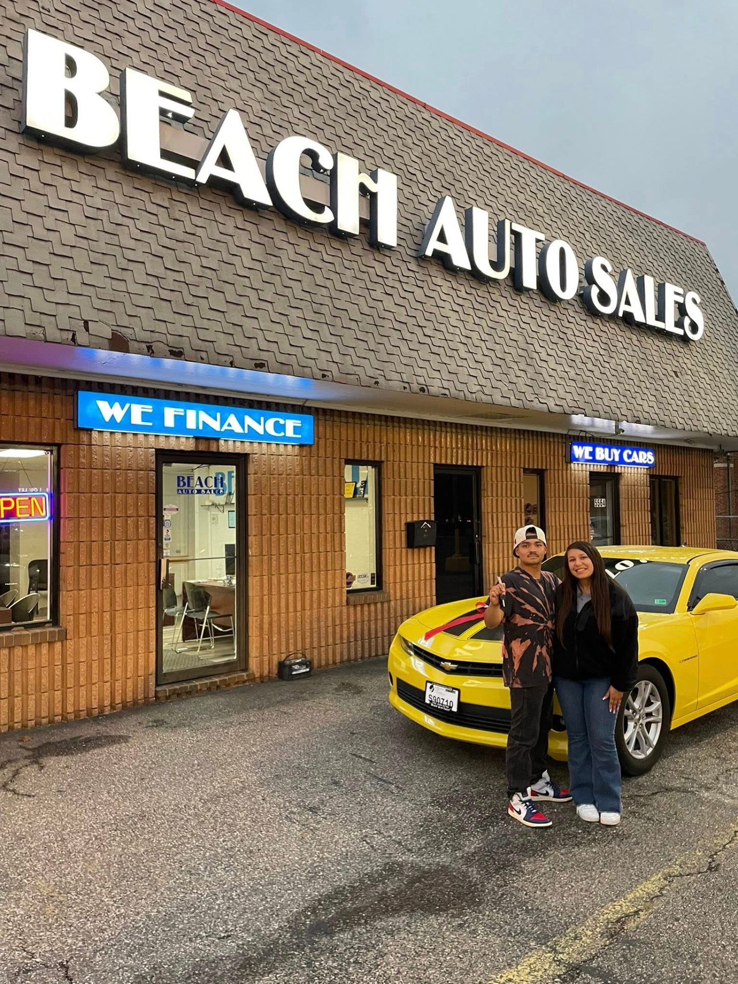 Happy customers at Beach Auto Sales storefront on Virginia Beach Boulevard with their new Camaro